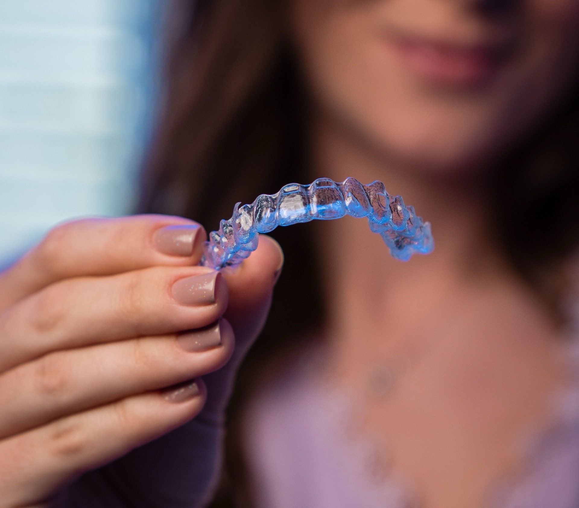 Clear aligner held by a smiling patient